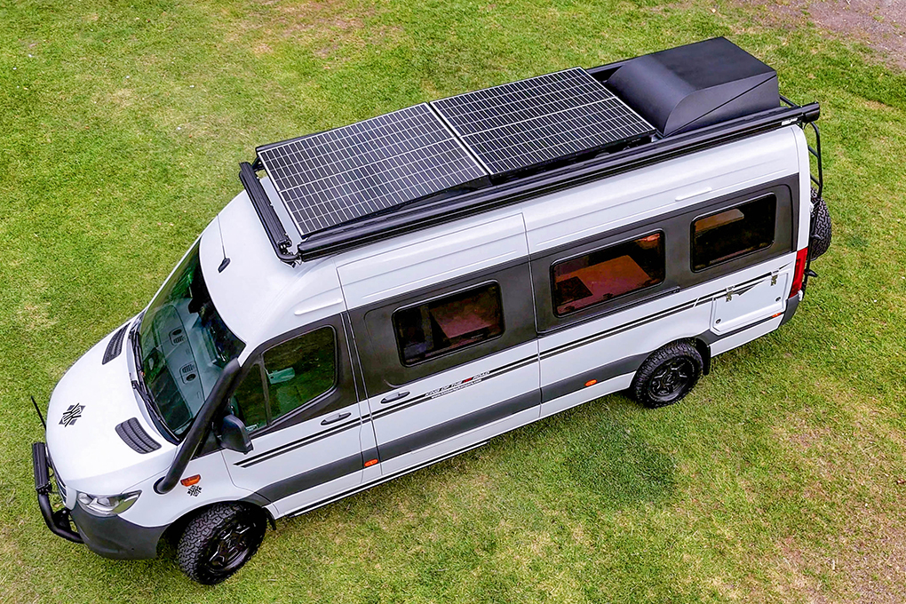 Off-road motorhome camper van with solar panels on roof parked on grass.