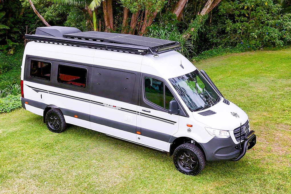 Off-road motorhome camper van with solar panels on roof parked on grass.